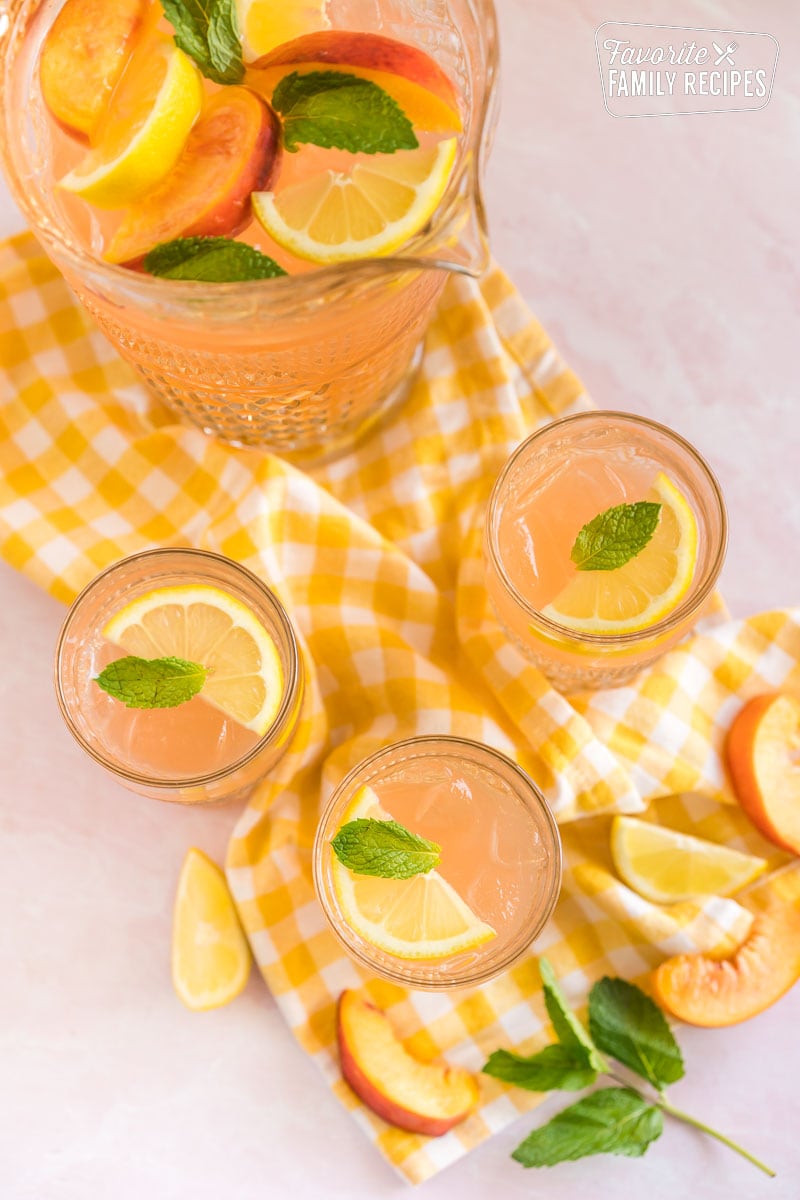 Three glasses of peach lemonade topped with lemon slices and mint leaves.