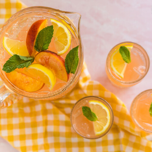 A pitcher of peach lemonade topped with peach slices, lemons, and mint leaves