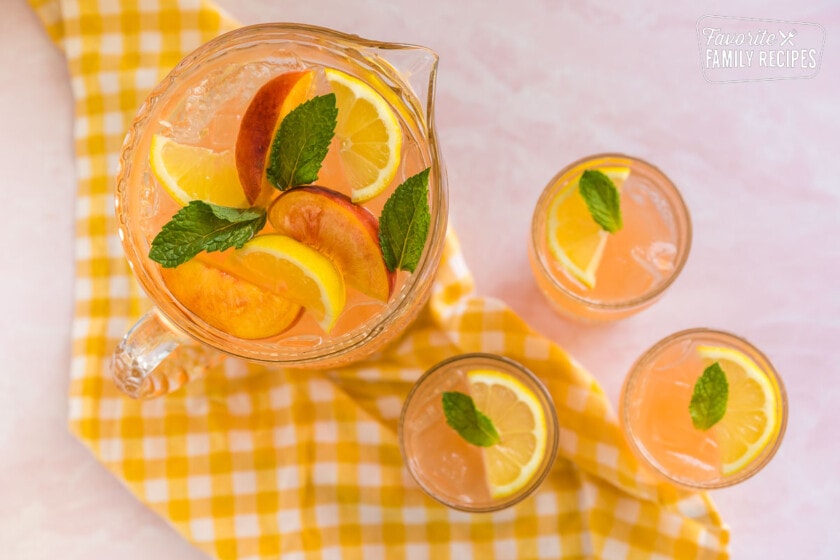 A pitcher of peach lemonade topped with peach slices, lemons, and mint leaves