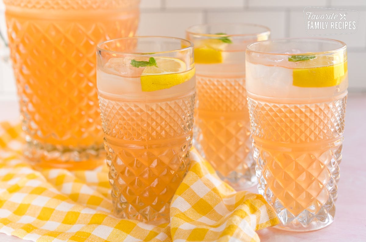 Three glasses of peach lemonade topped with lemon slices and mint leaves.