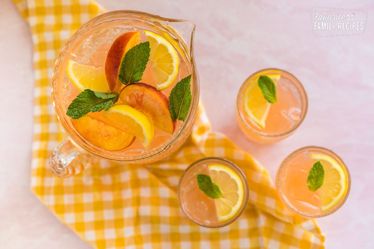 A pitcher of peach lemonade topped with peach slices, lemons, and mint leaves.