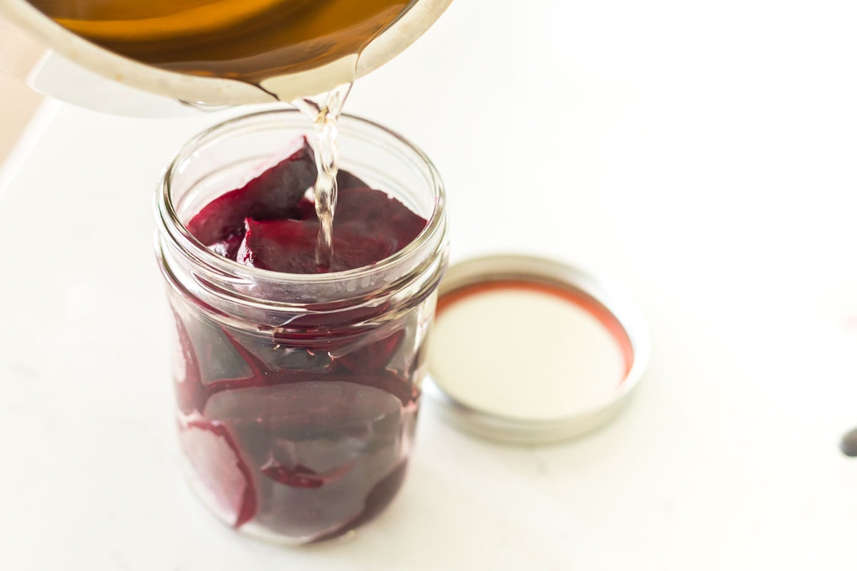 Sugar water being poured into a jar with cooked, sliced beets.