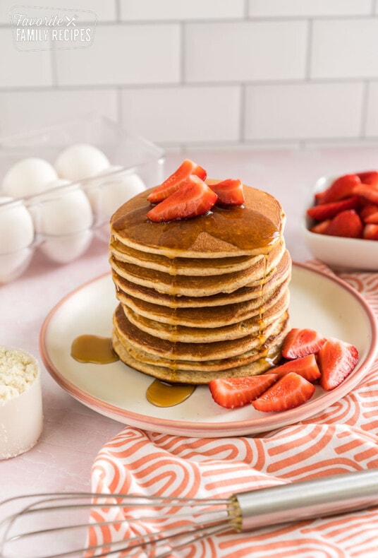 A stack of protein pancakes with strawberries on top and maple syrup dripping down the side