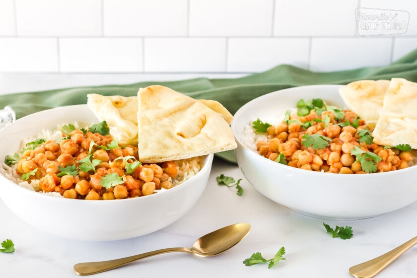 Two bowls side by side of Curried Chickpeas. Garnished with cilantro and sliced Naan Bread.