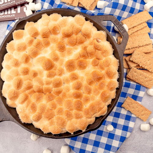 S'mores dip in a cast iron skillet surrounded by graham crackers, mini marshmallows, and hershey's bars