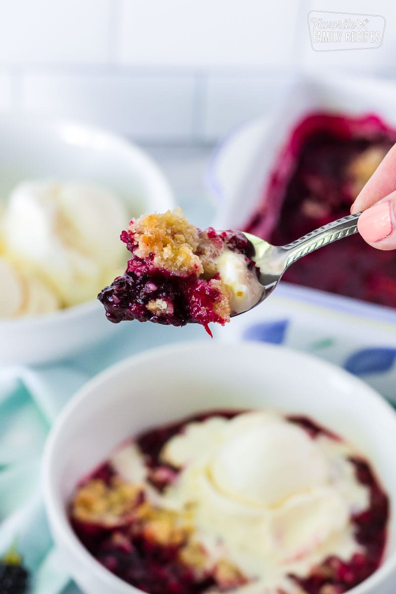 Hand holding up a spoon full of Easy Blackberry Cobbler.