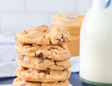 Tall stack of six Peanut Butter Chocolate Chip Cookies on a square of parchment paper. Glass of milk served on the side.
