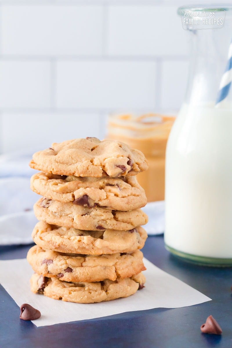 Tall stack of six Peanut Butter Chocolate Chip Cookies on a square of parchment paper. Glass of milk served on the side.