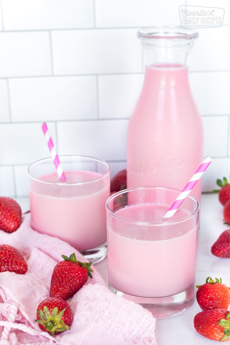 A pitcher of strawberry milk next to two full glasses