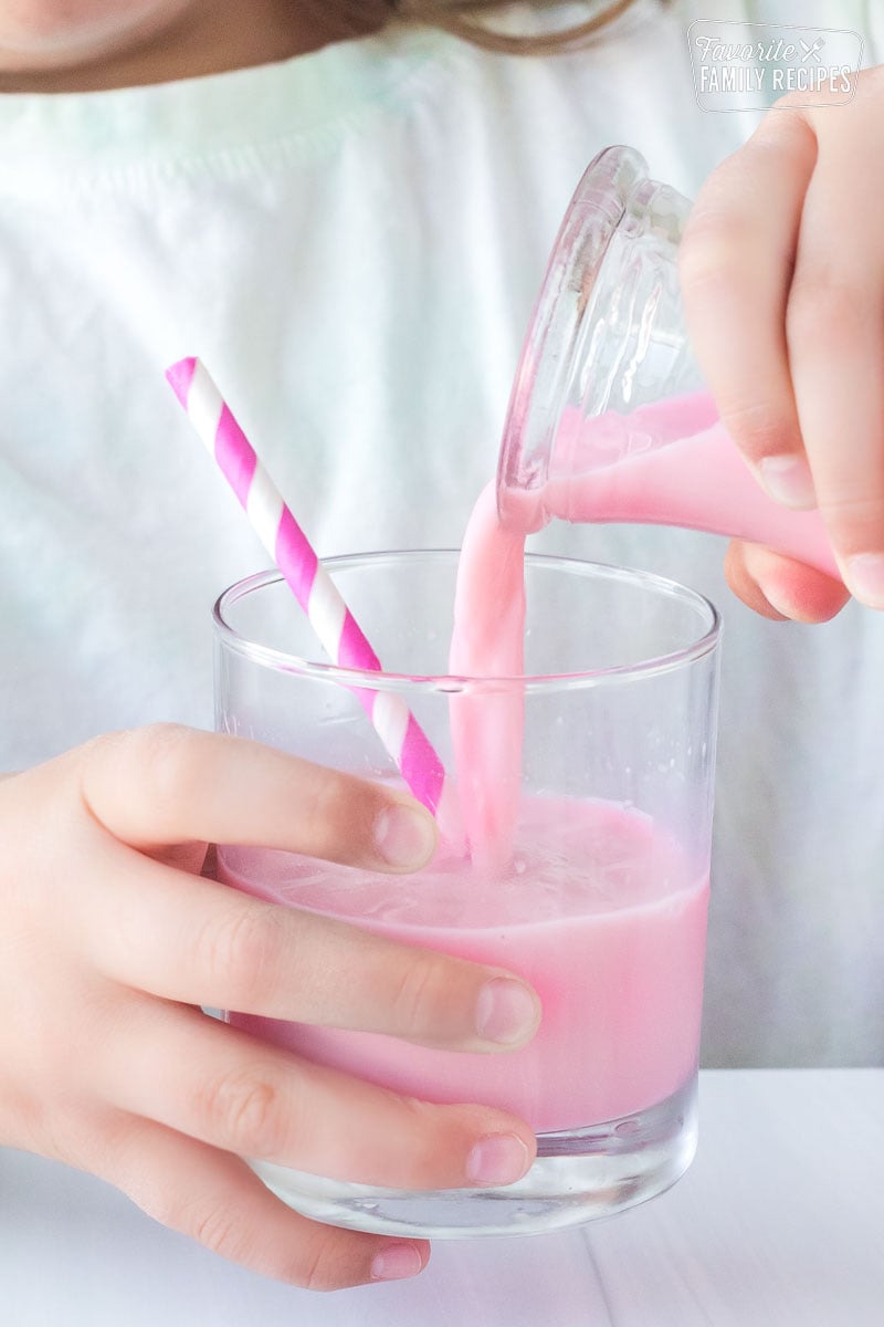 strawberry milk being poured from a pitcher into a glass