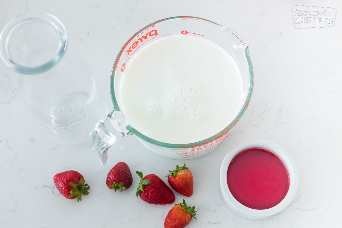 Milk in a liquid measuring cup with a cup of strawberry syrup next to it