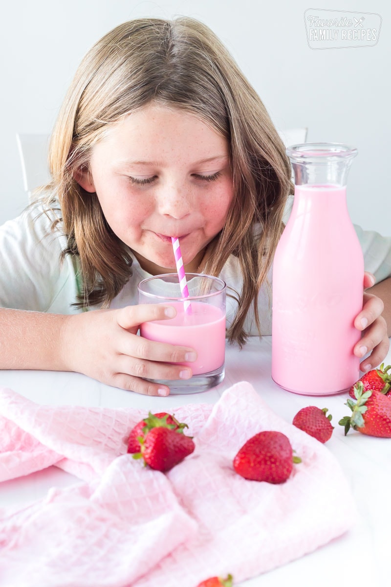 A girl drinking strawberry milk through a straw.