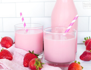 Pink strawberry milk in two glasses with a pitcher of milk behind them
