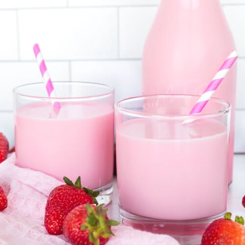 Pink strawberry milk in two glasses with a pitcher of milk behind them