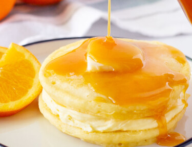 Orange Syrup pouring on top of two Orange Pancakes.