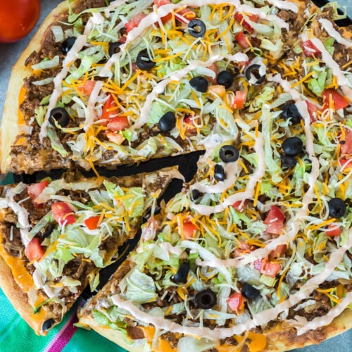 A slice of taco pizza being lifted from a whole pizza