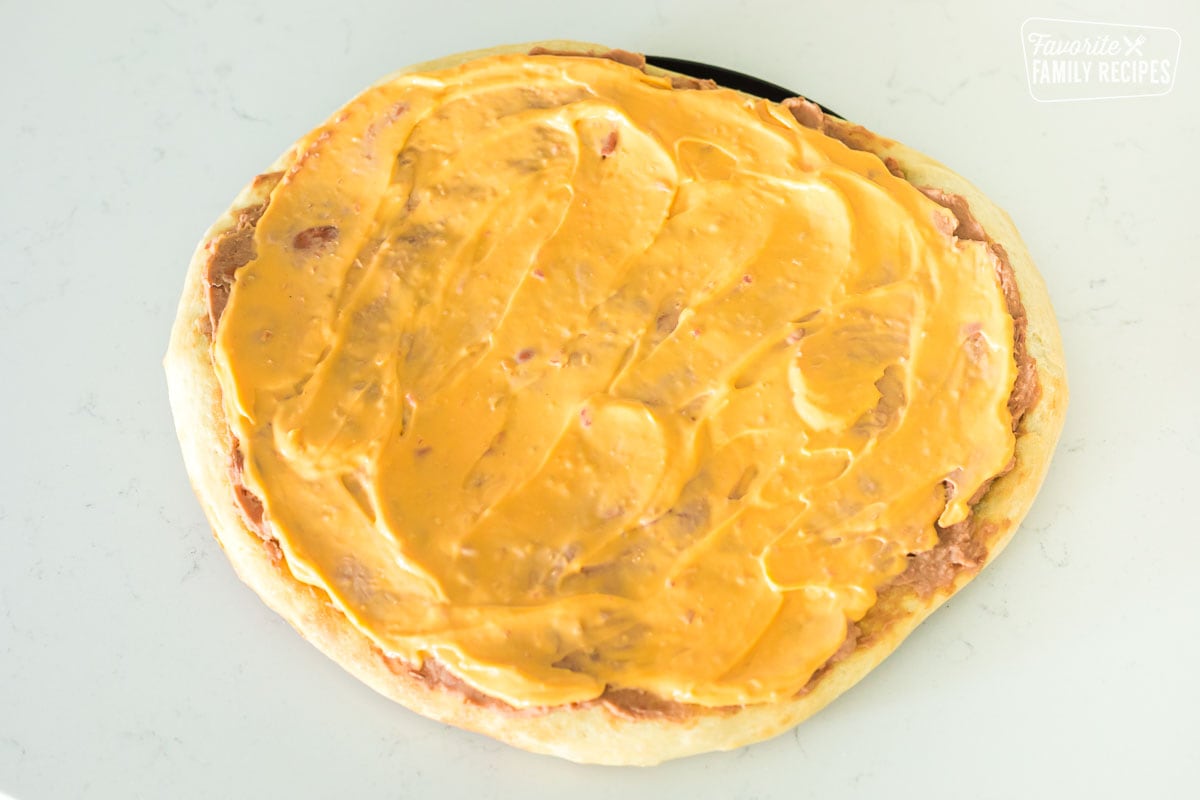 Nacho cheese spread as a layer on a taco pizza.