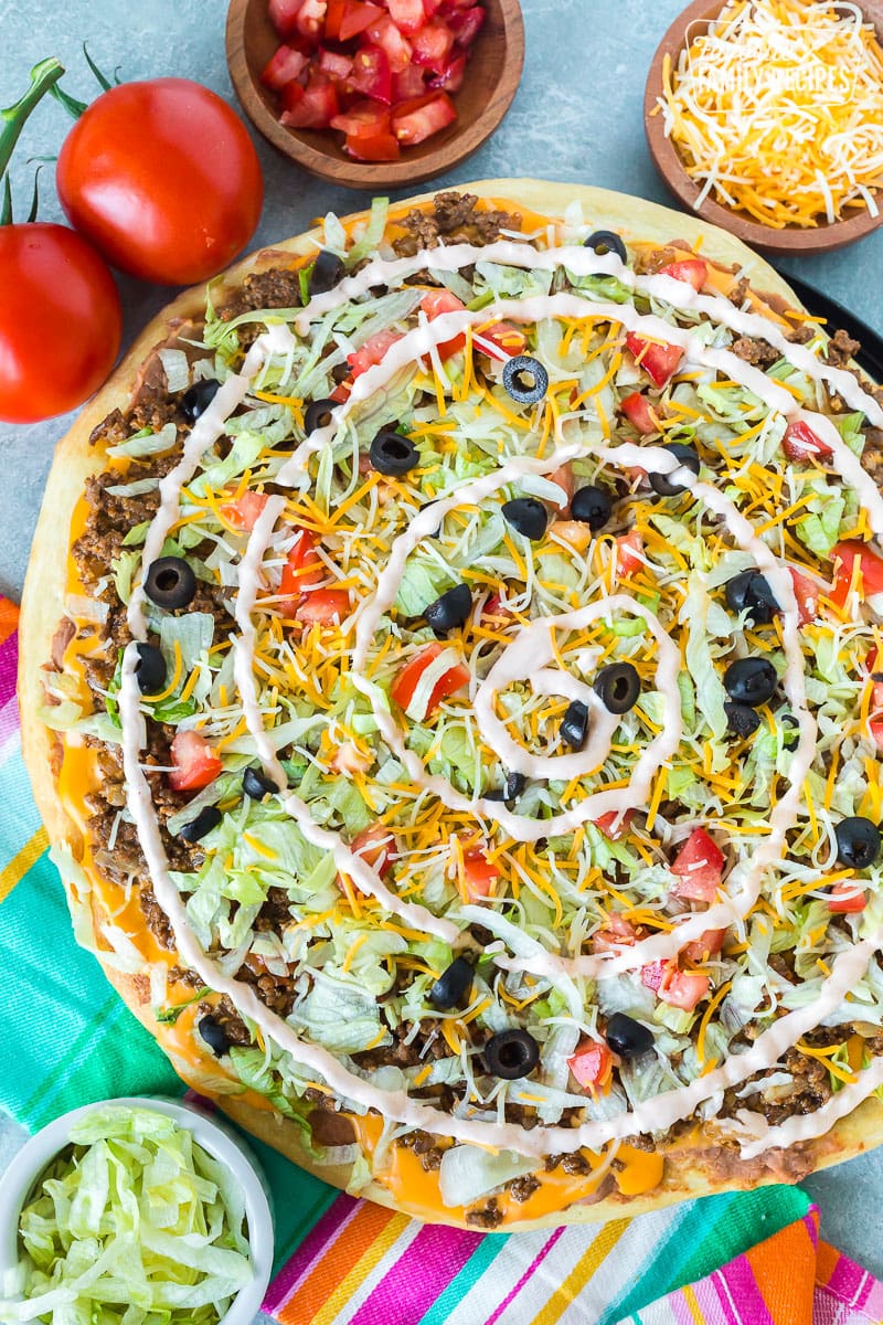A top view of a taco pizza showing toppings and a swirl of sour cream sauce.
