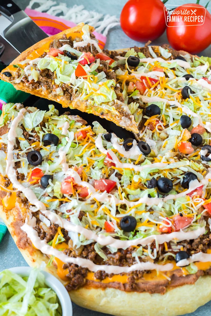 A taco pizza on a pizza stone with a slice being taken from it.