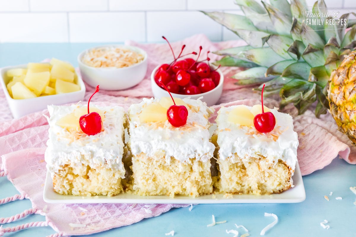 Three slices of Pina Colada Cake side by side. Garnished with cherries, pineapple and toasted coconut.