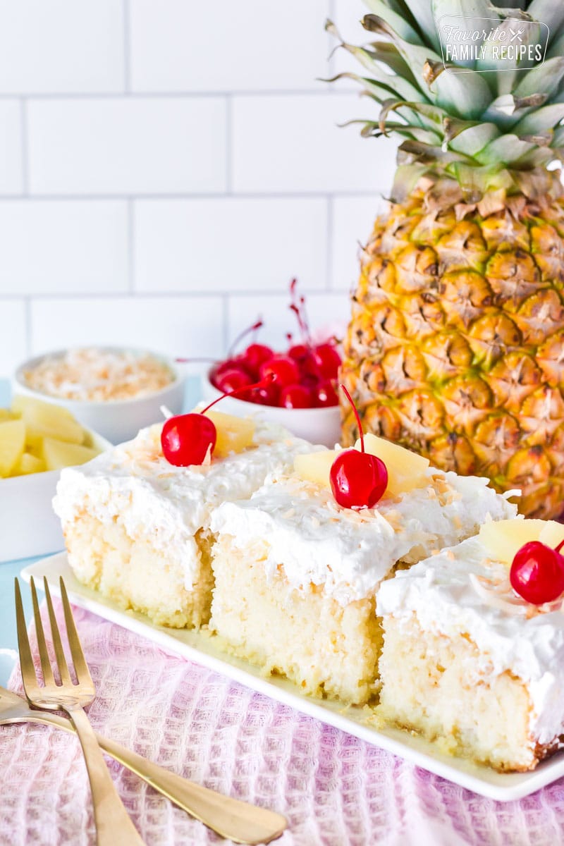 Three slices of Pina Colada Cake in a row. Fresh pineapple, cherries and toasted coconut on the side.