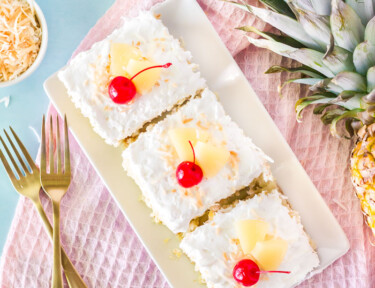 Top view of three slices of Pina Colada Cake. Garnished with cherries, sliced pineapple and toasted coconut.