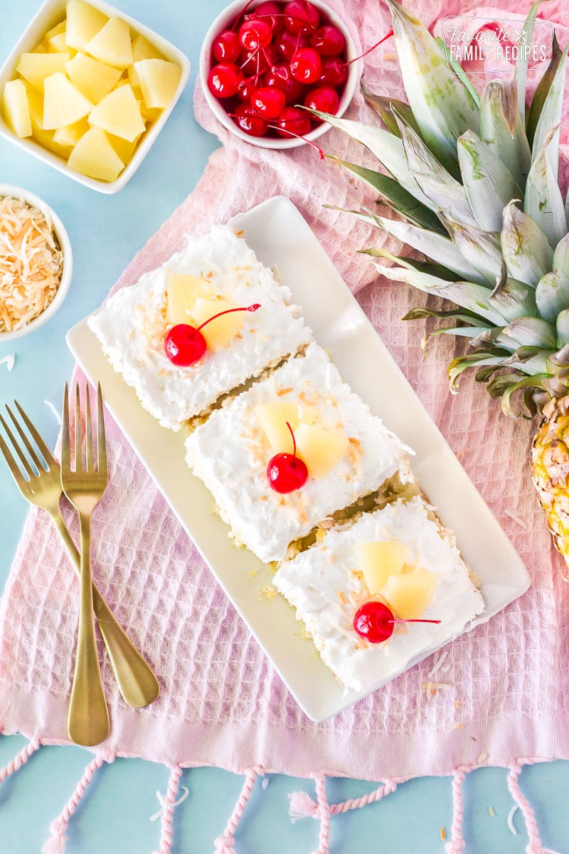 Top view of three slices of Pina Colada Cake. Garnished with cherries, sliced pineapple and toasted coconut.