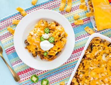 Frito Chili Pie on a plate with the serving tray to the side. Bag of Fritos with chips coming out on the side.
