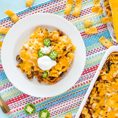 Frito Chili Pie on a plate with the serving tray to the side. Bag of Fritos with chips coming out on the side.
