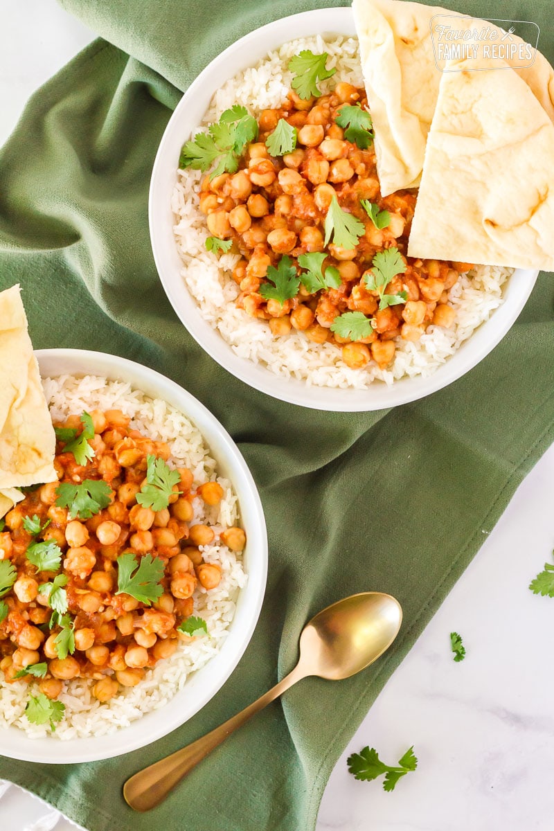 Two bowls of Curried Chickpeas over rice and sliced Naan bread on the side.
