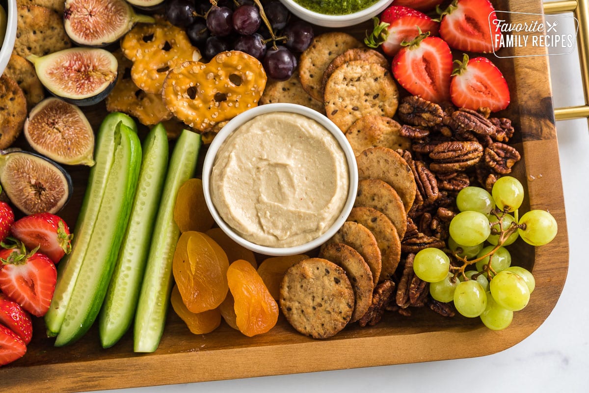 A bowl of hummus surrounded by crackers, fruits, and veggies.