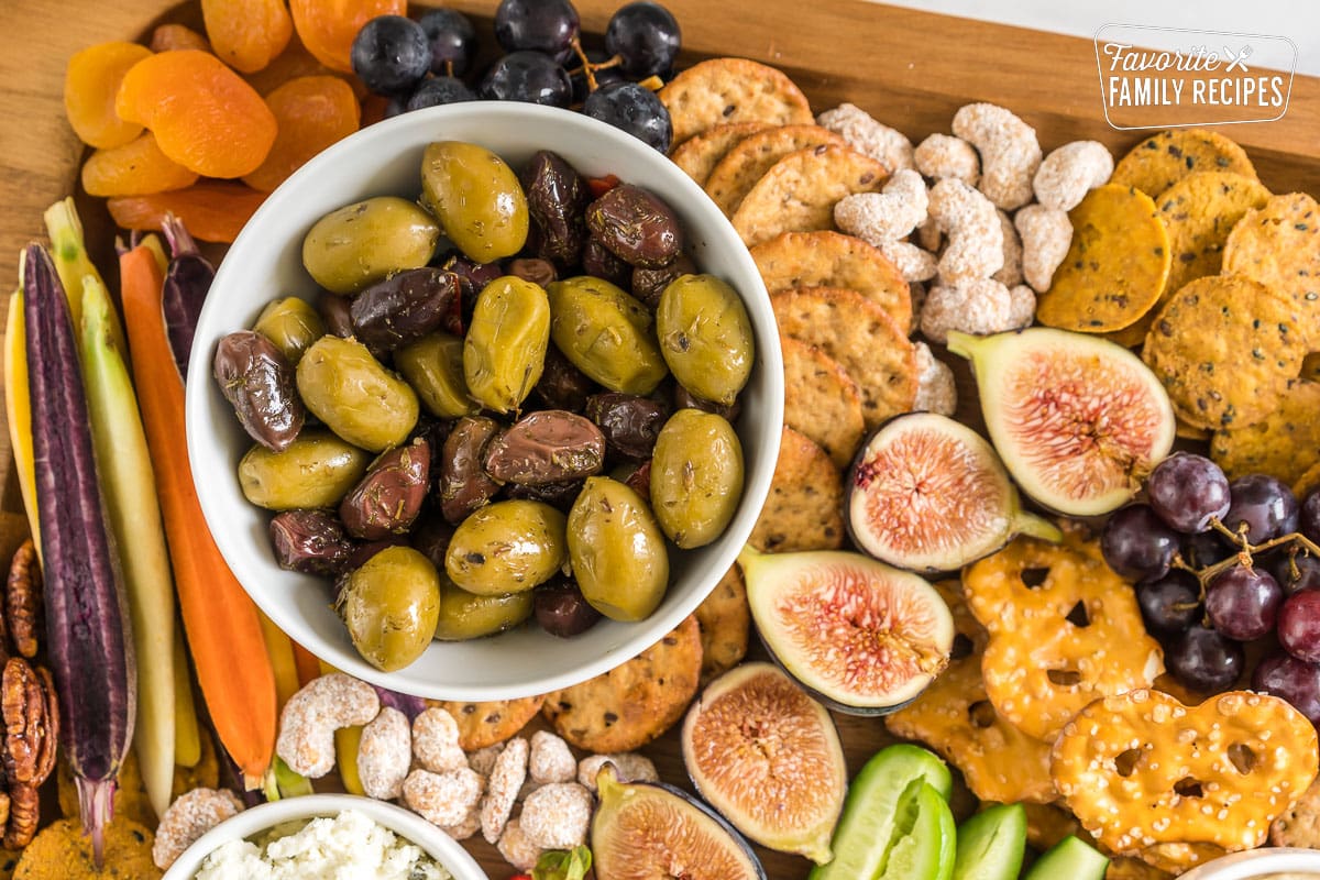 A bowl of marinated olives on a charcuterie board.