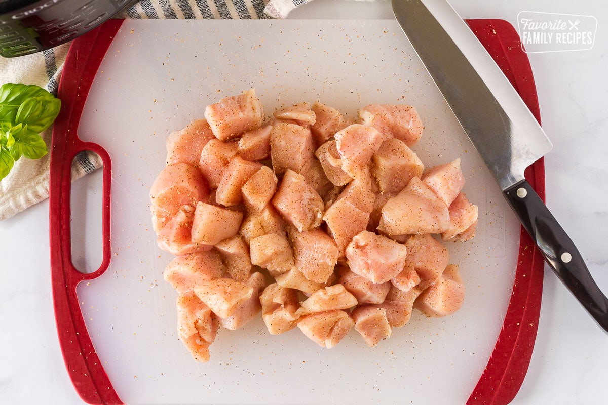 Cubed raw chicken breast on a cutting board with a knife to make Instant Pot Chicken and Rice.