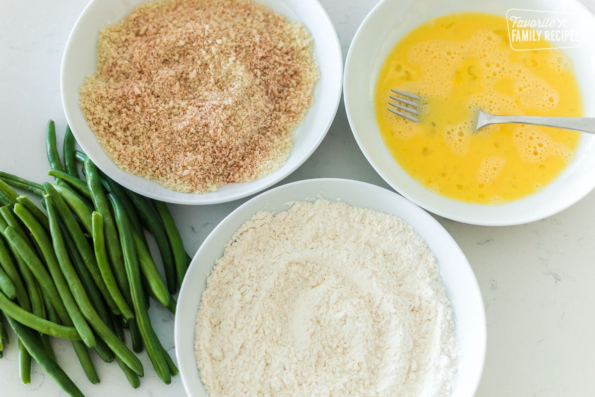 Ingredients to make air fryer green beans including breadcrumbs, eggs, green beans, and flour.