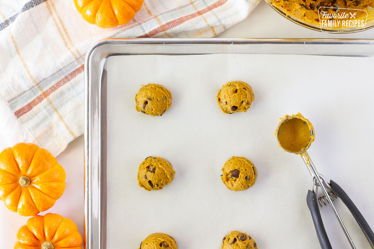 Cookie sheet with a cookie scoop and balls of Pumpkin Chocolate Chip Cookie dough.