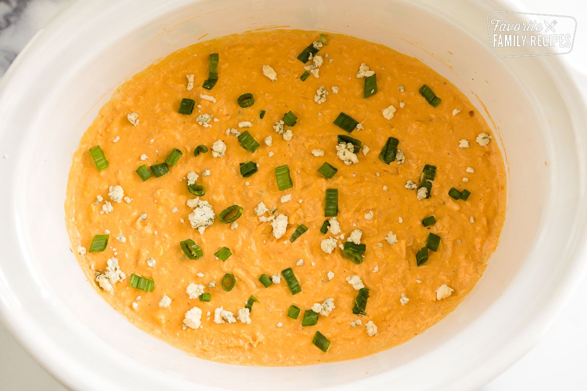 Buffalo chicken dip in a crock pot topped with green onions and blue cheese