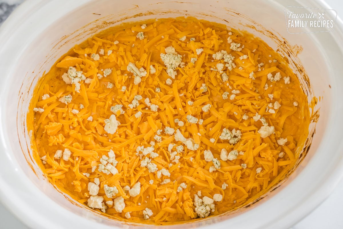Buffalo chicken dip in a crock pot topped with shredded cheddar cheese and blue cheese.