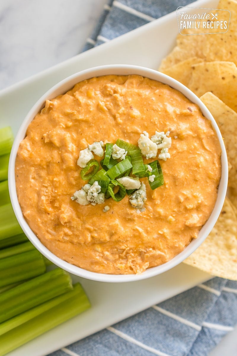 This Crock pot buffalo chicken dip recipe is the perfect appetizer for your next party. It is made with Frank's Hot Sauce and cheddar cheese. A small bowl of buffalo chicken dip topped with green onions and blue cheese.