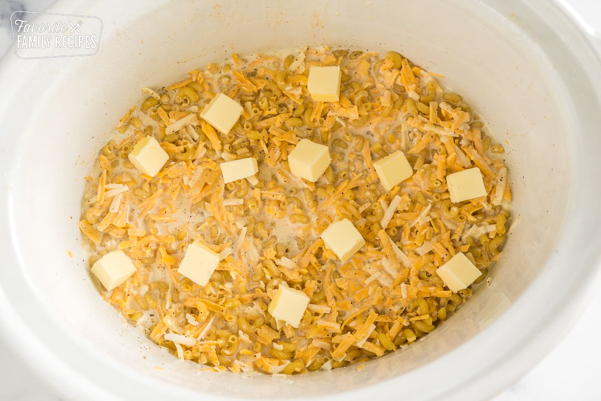 noodles, milk, and cheese in a crock pot topped with butter