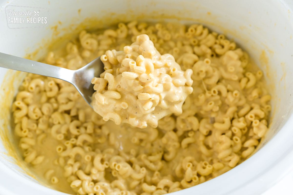 A scoop of mac and cheese taken from a crock pot.