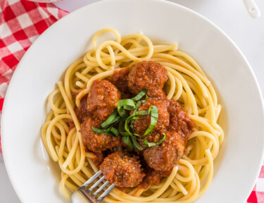 A plate of spaghetti topped with meatballs from a crockpot and basil