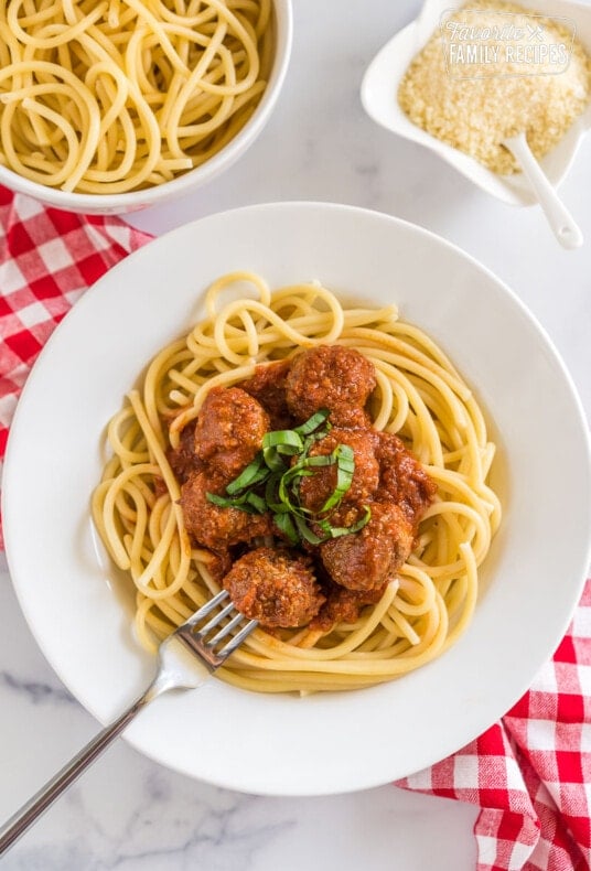 A plate of spaghetti topped with meatballs from a crockpot and basil