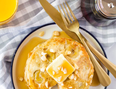 Stack of Banana Pancakes on a plate missing a slice. Silverware on the plate.