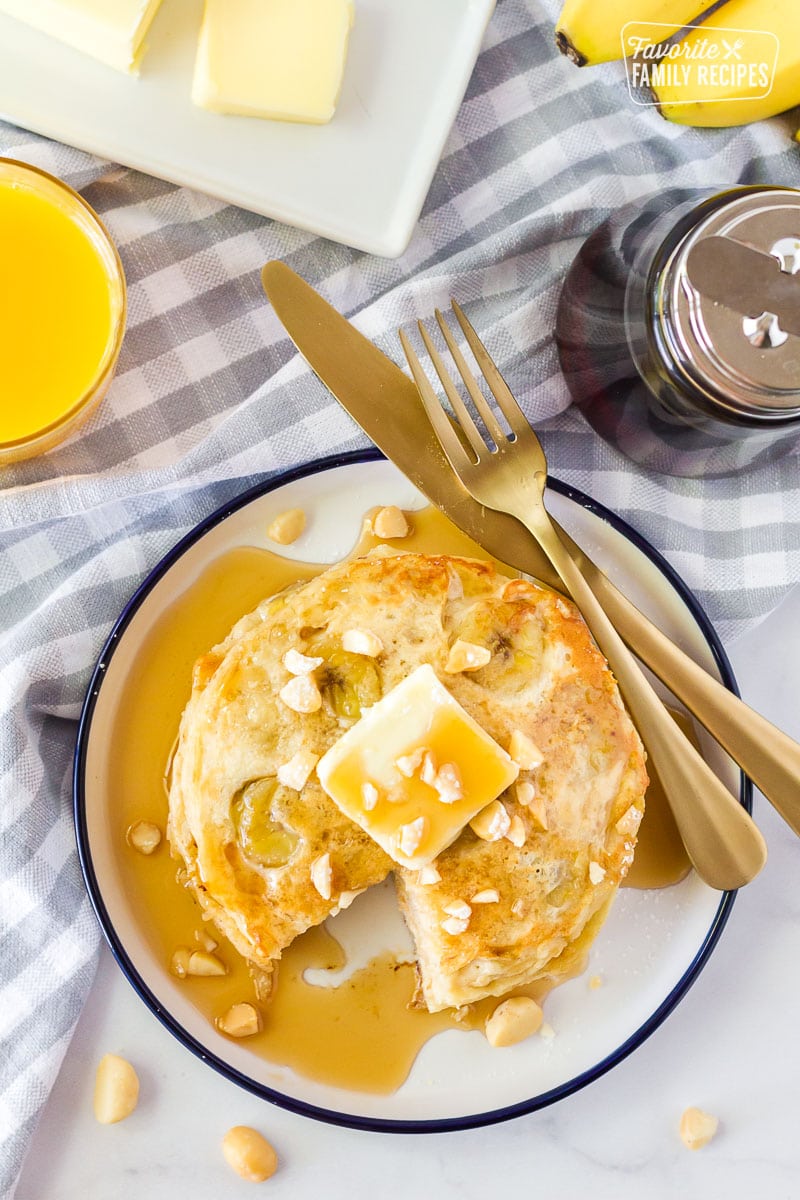 Stack of Banana Pancakes on a plate missing a slice. Silverware on the plate.