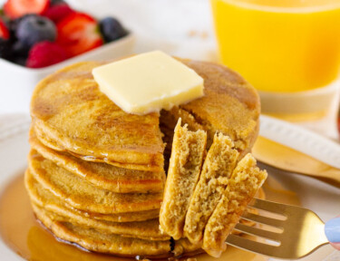 Fork with three pieces of Whole Wheat Pancakes. Fruit and juice on the side.