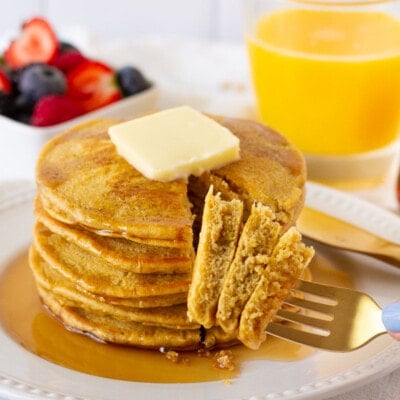 Fork with three pieces of Whole Wheat Pancakes. Fruit and juice on the side.