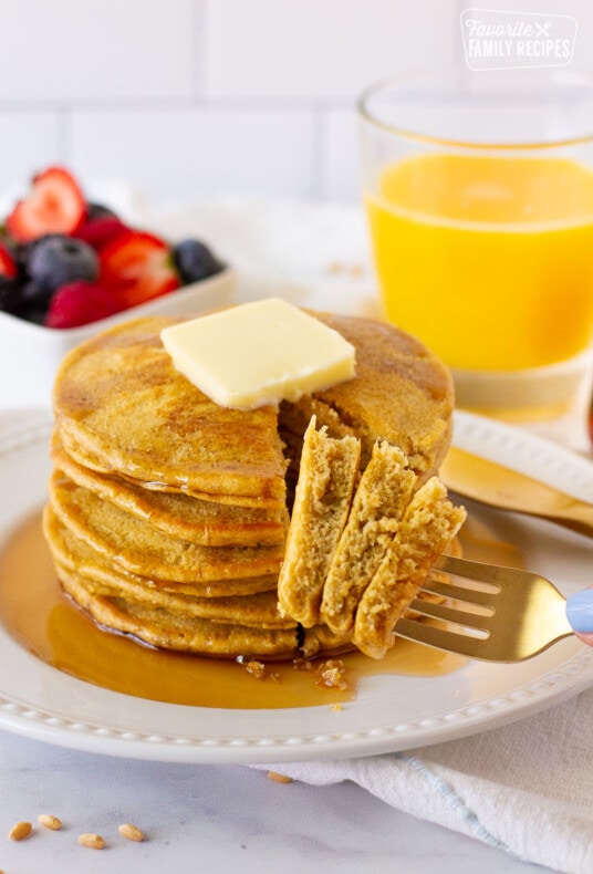Fork with three pieces of Whole Wheat Pancakes. Fruit and juice on the side.
