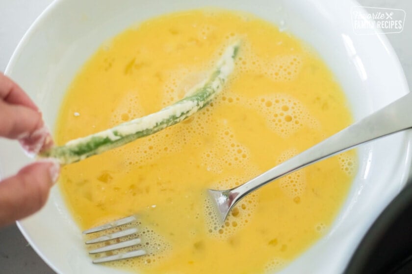 A green bean being dipped in an egg mixture to make air fryer green beans