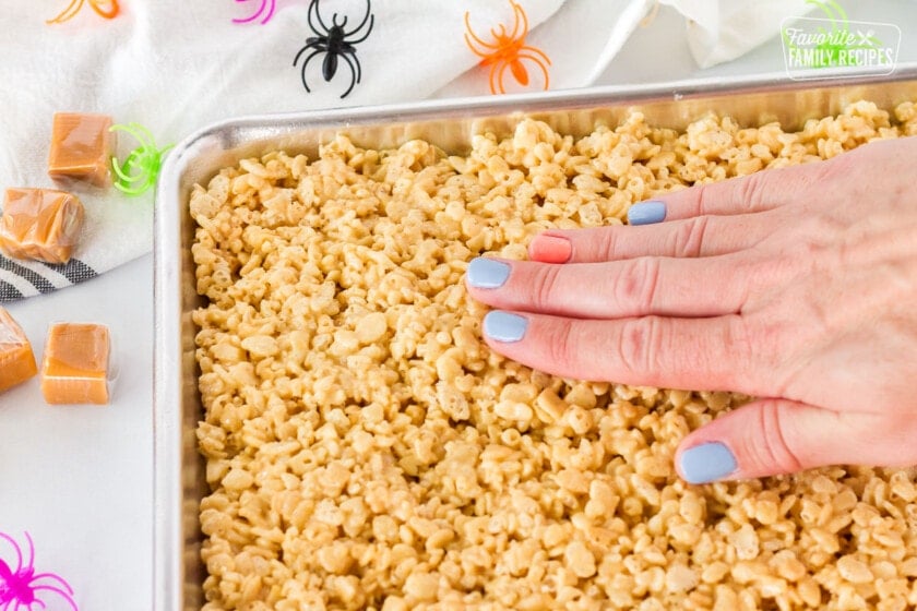 Hand pressing down on Halloween Rice Krispie Treats.