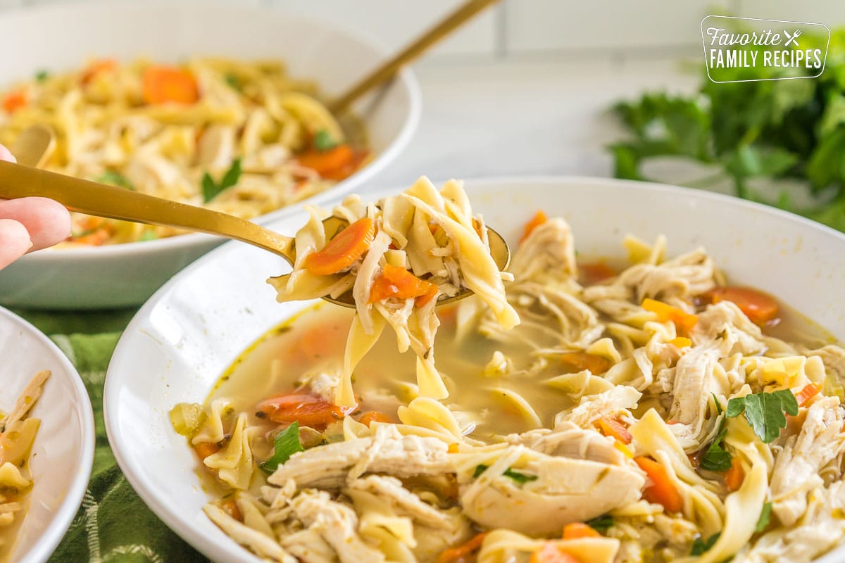 A bowl of chicken noodle soup with a spoonful being taken out.